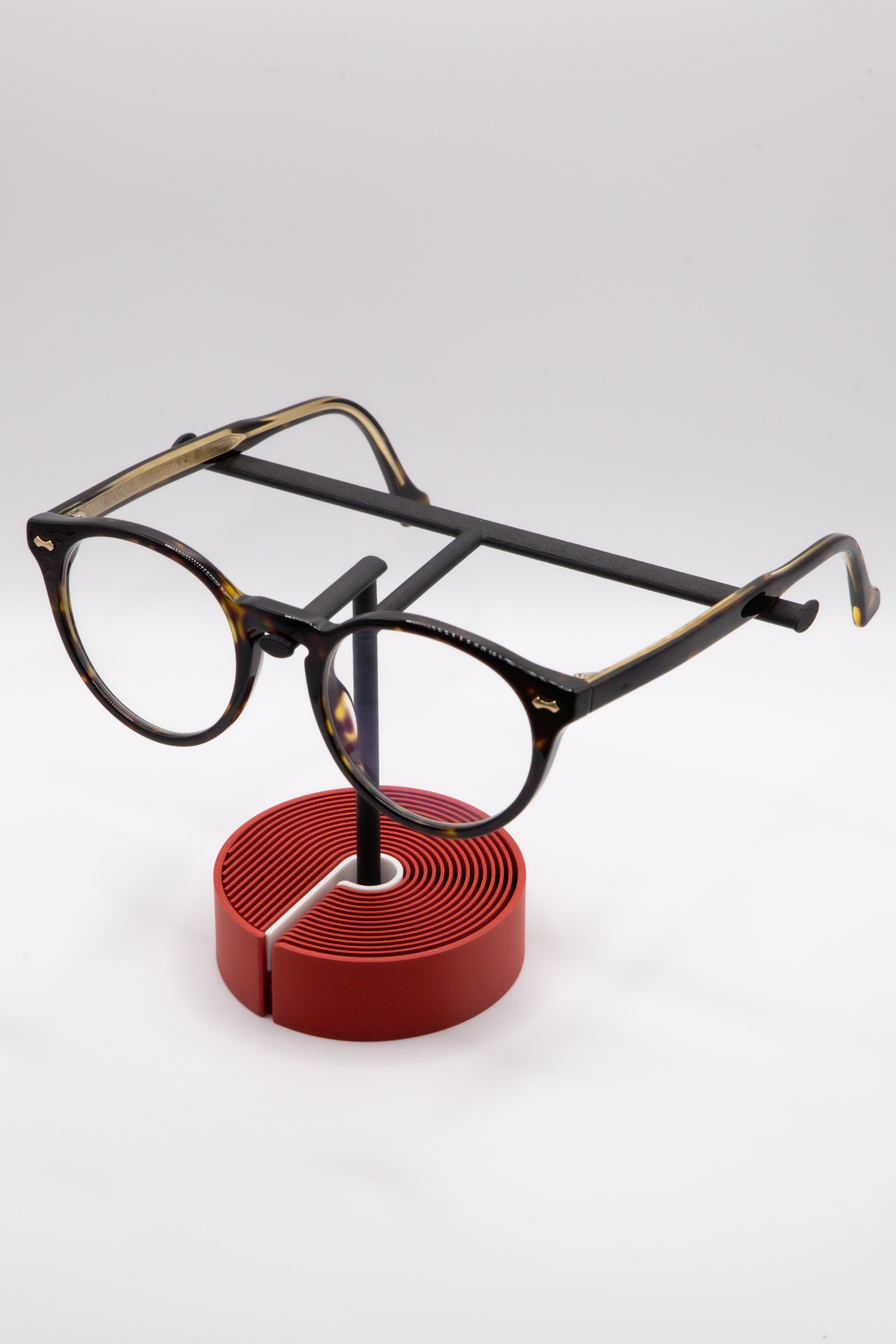 Brillenhalter PureStand in Schwarz matt mit runder roter Base, weissem Einlegeteil und Brille aufgesetzt.