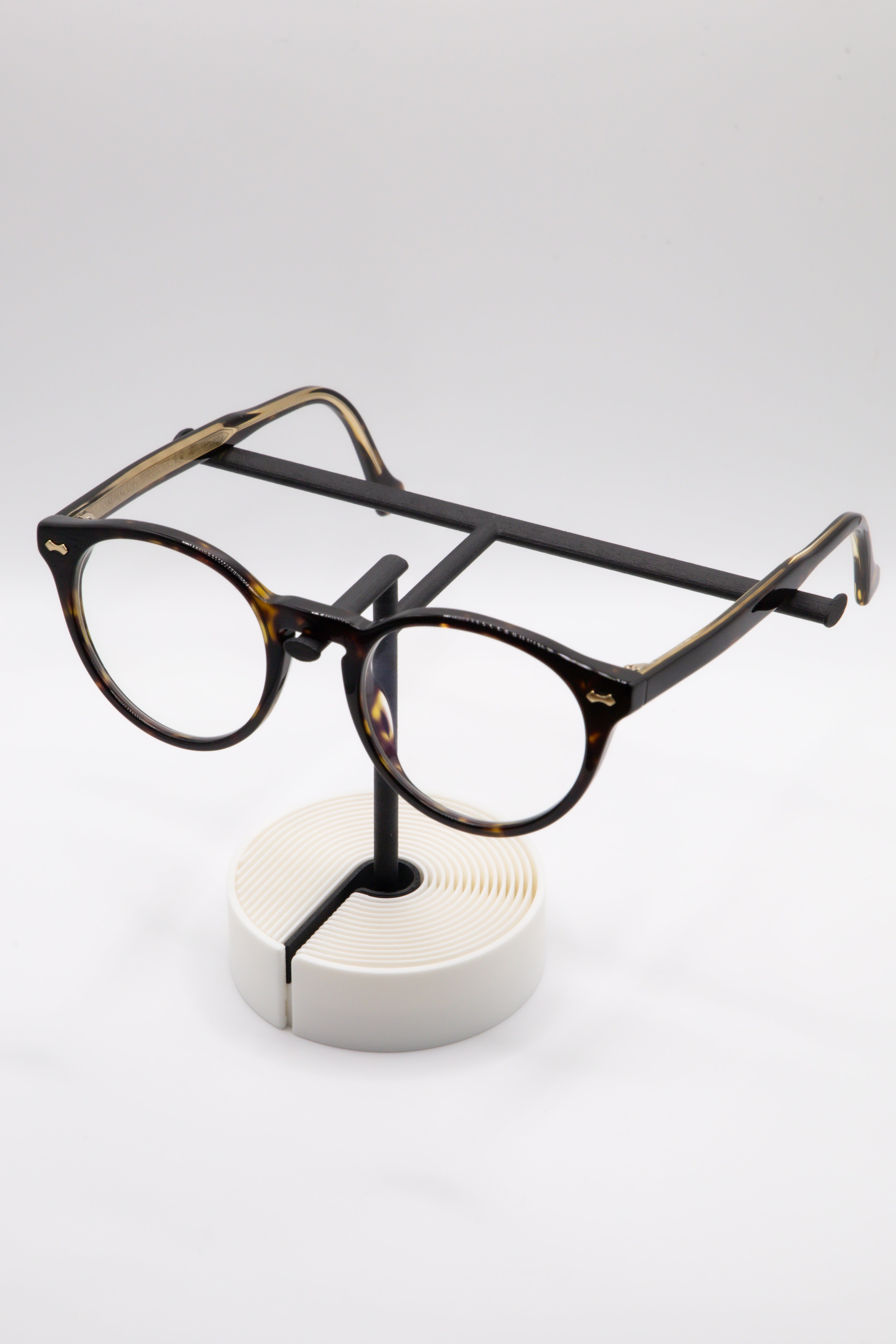 Brillenhalter PureStand in Schwarz matt mit runder weisser Base, schwarzem Einlegeteil und Brille aufgesetzt.