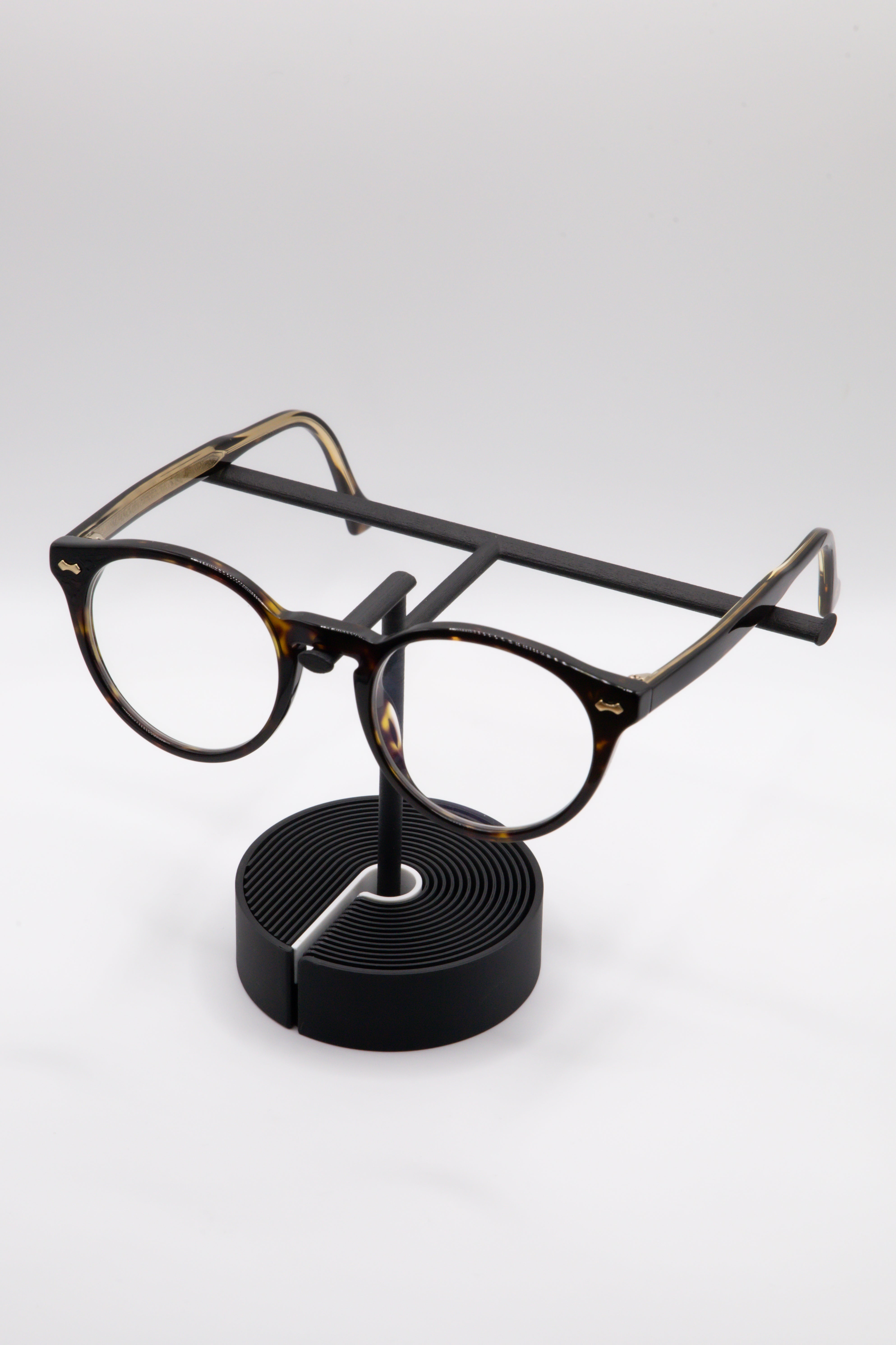 Brillenhalter PureStand in Schwarz matt mit runder schwarzer Base, weissem Einelegeteil und Brille aufgesetzt.