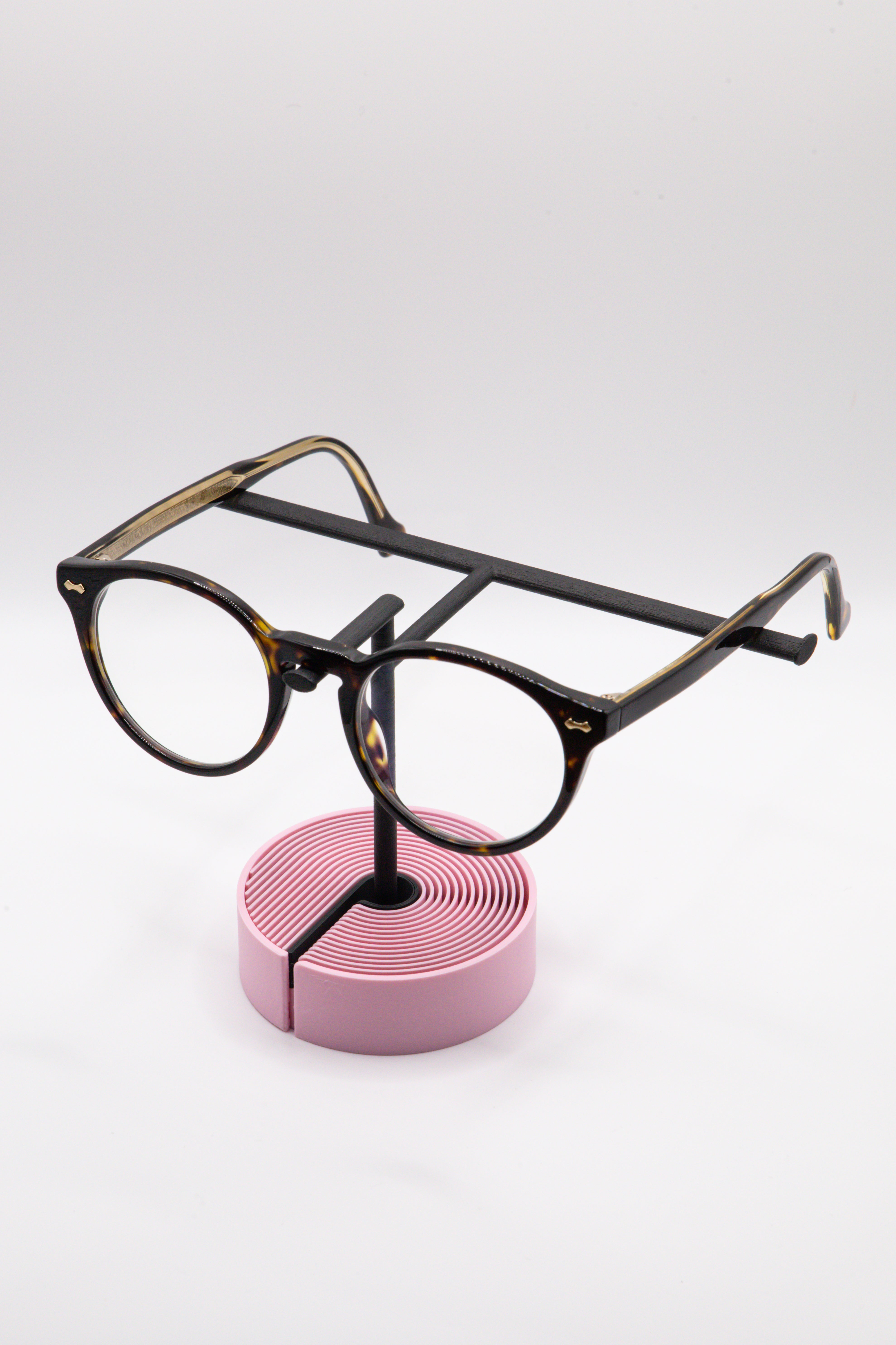 Brillenhalter PureStand in Schwarz matt mit runder pinker Base, schwarzem Einlegeteil und Brille aufgesetzt.