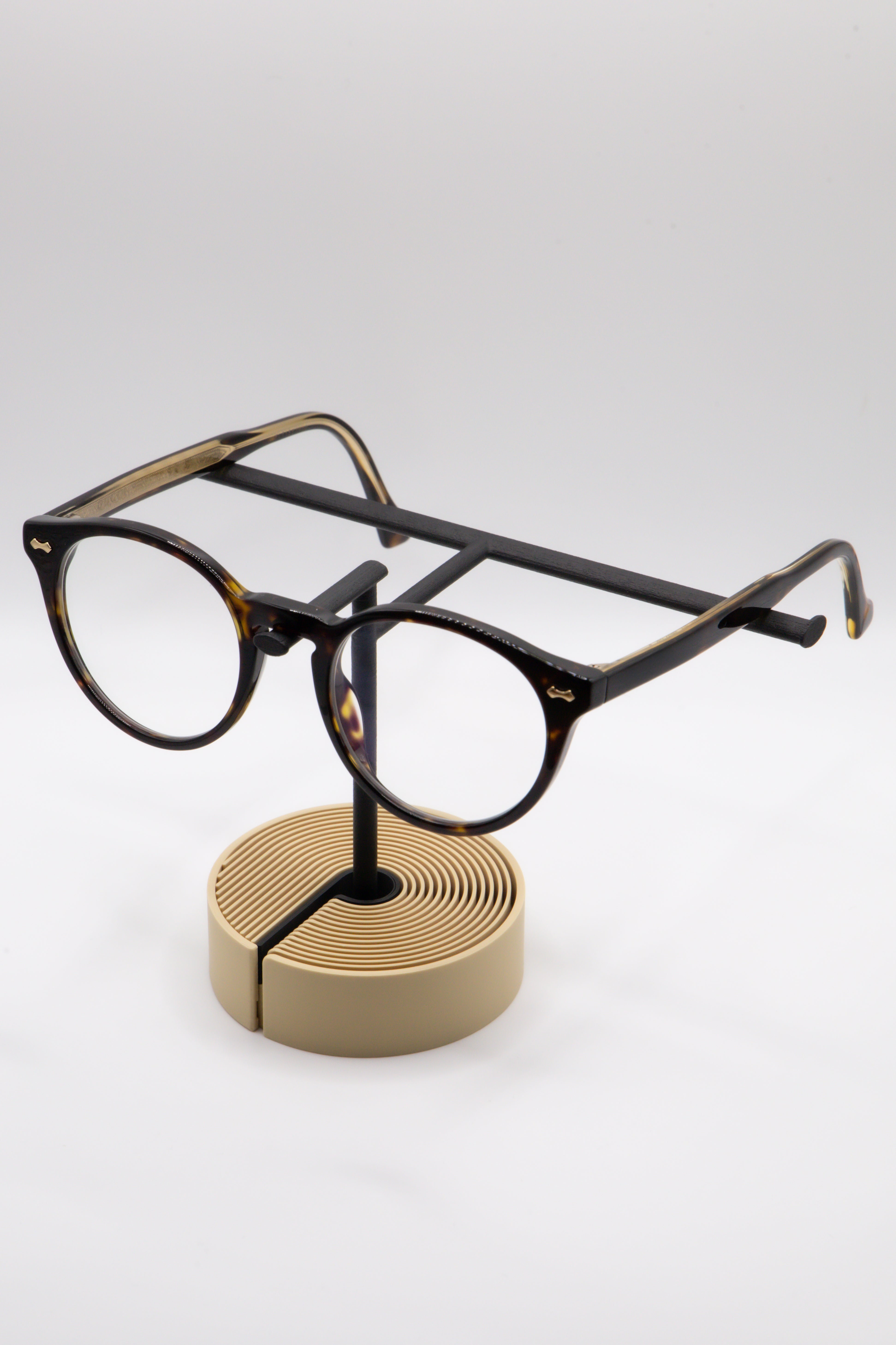 Brillenhalter PureStand in Schwarz matt mit runder beiger Base, schwarzem Einlegeteil und Brille aufgesetzt.
