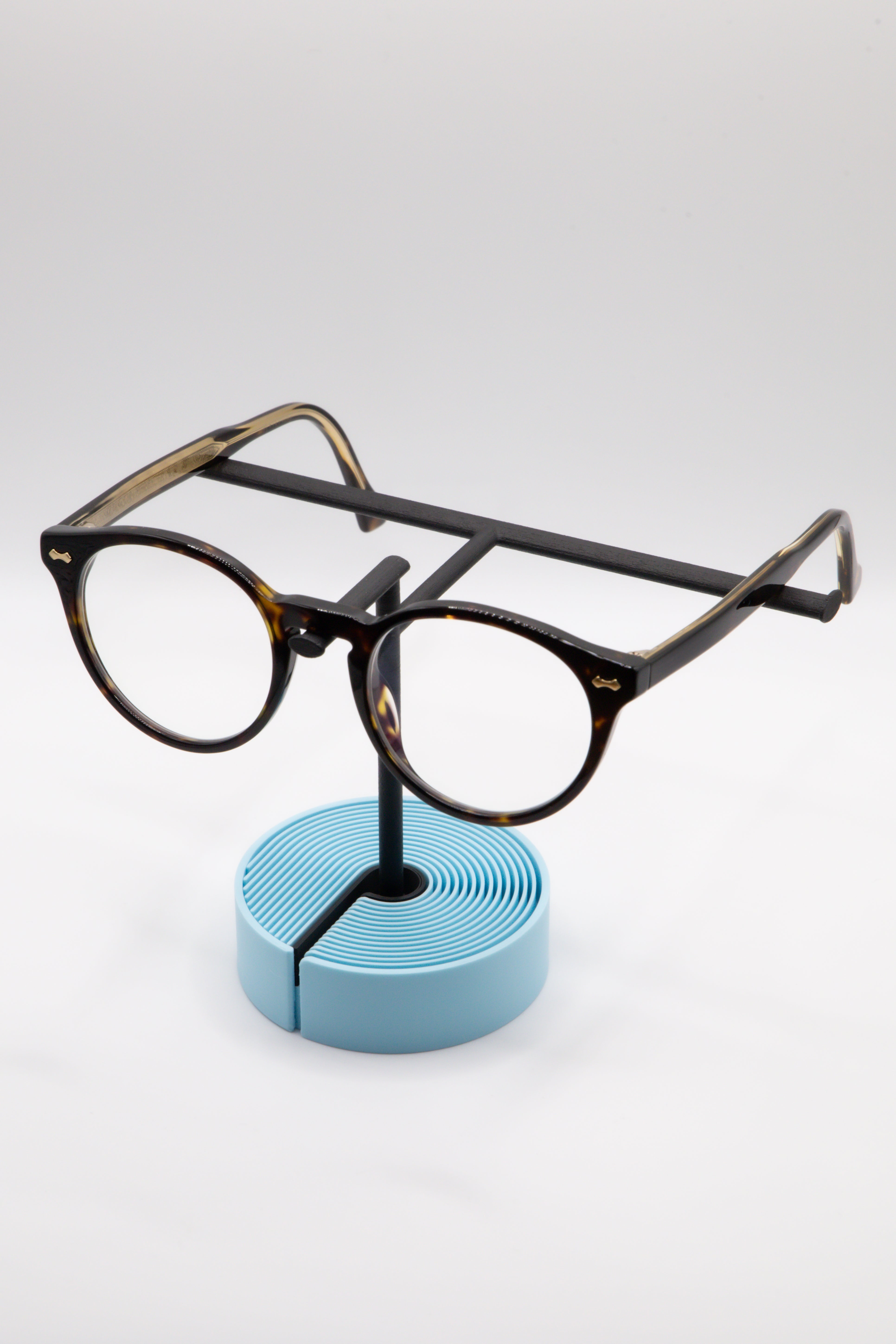Brillenhalter PureStand in Schwarz matt mit runder blauer Base, schwarzem Einlegeteil und Brille aufgesetzt.